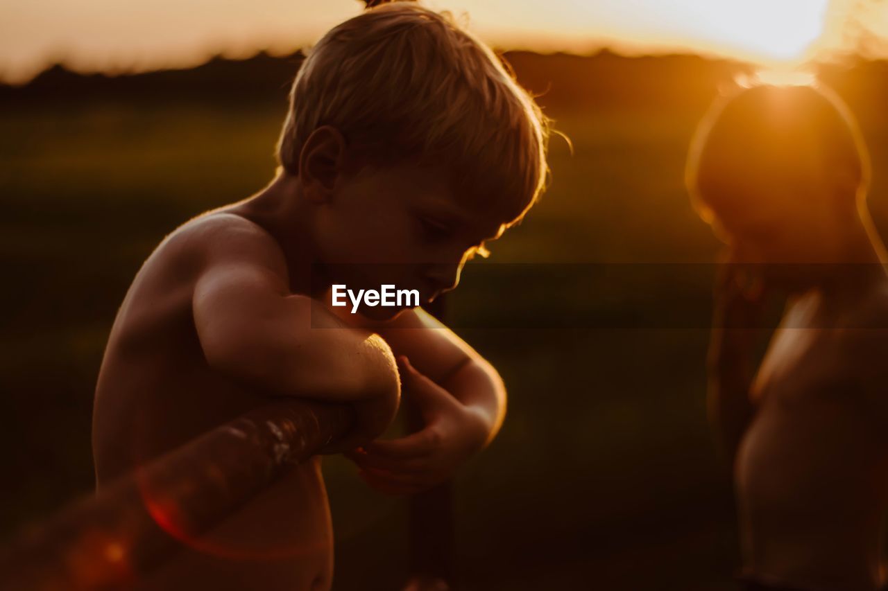 Side view of shirtless boy on field during sunset