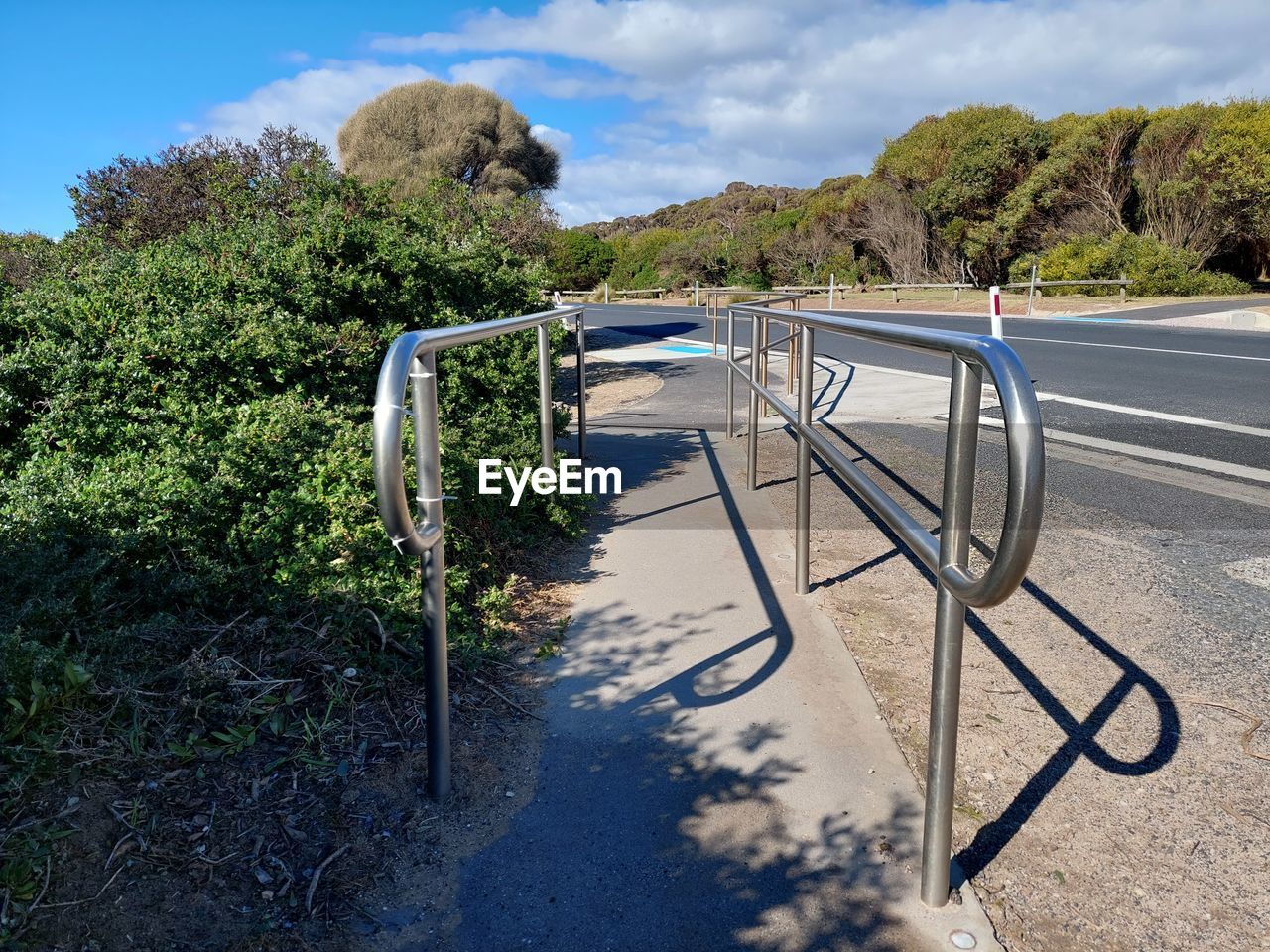 Empty road by railing against sky