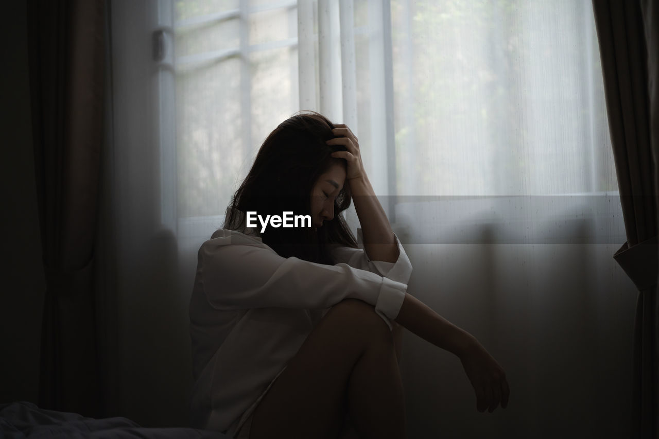 Frustrated woman sitting by window at home