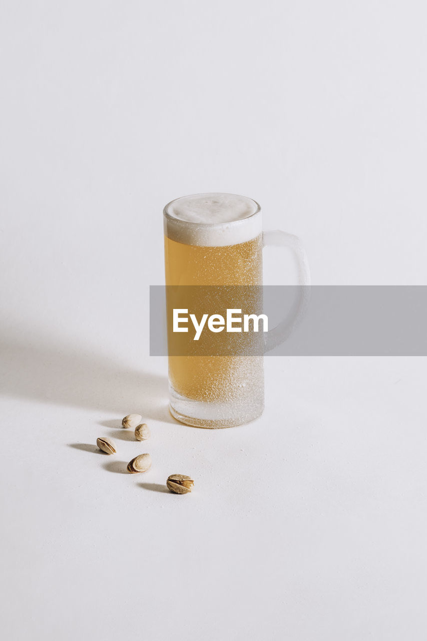 Chilled beer mug with frost on the surface and foam inside on a white background, pistachios