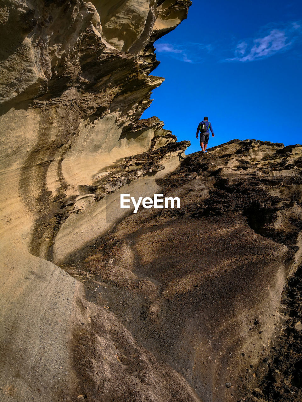 Low angle view of man climbing on rock against sky