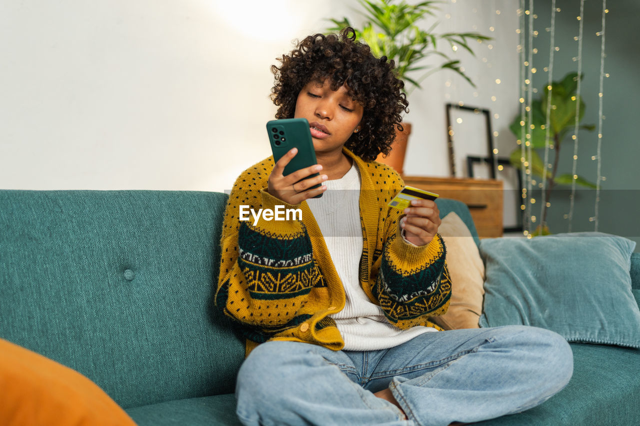 young woman using mobile phone while sitting on sofa