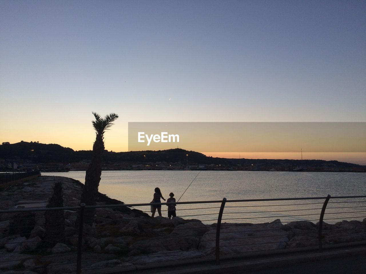 SILHOUETTE OF PEOPLE STANDING ON BEACH AT SUNSET