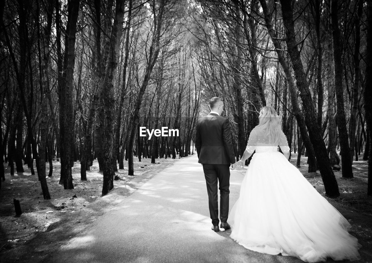 Rear view of wedding couple walking on road amidst trees