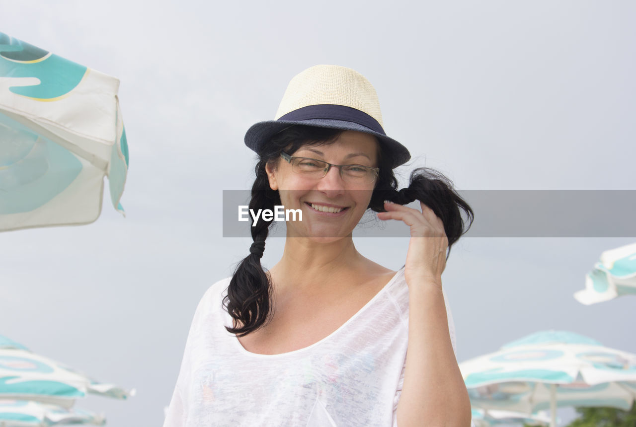 PORTRAIT OF HAPPY YOUNG WOMAN HOLDING HAT AGAINST WHITE BACKGROUND