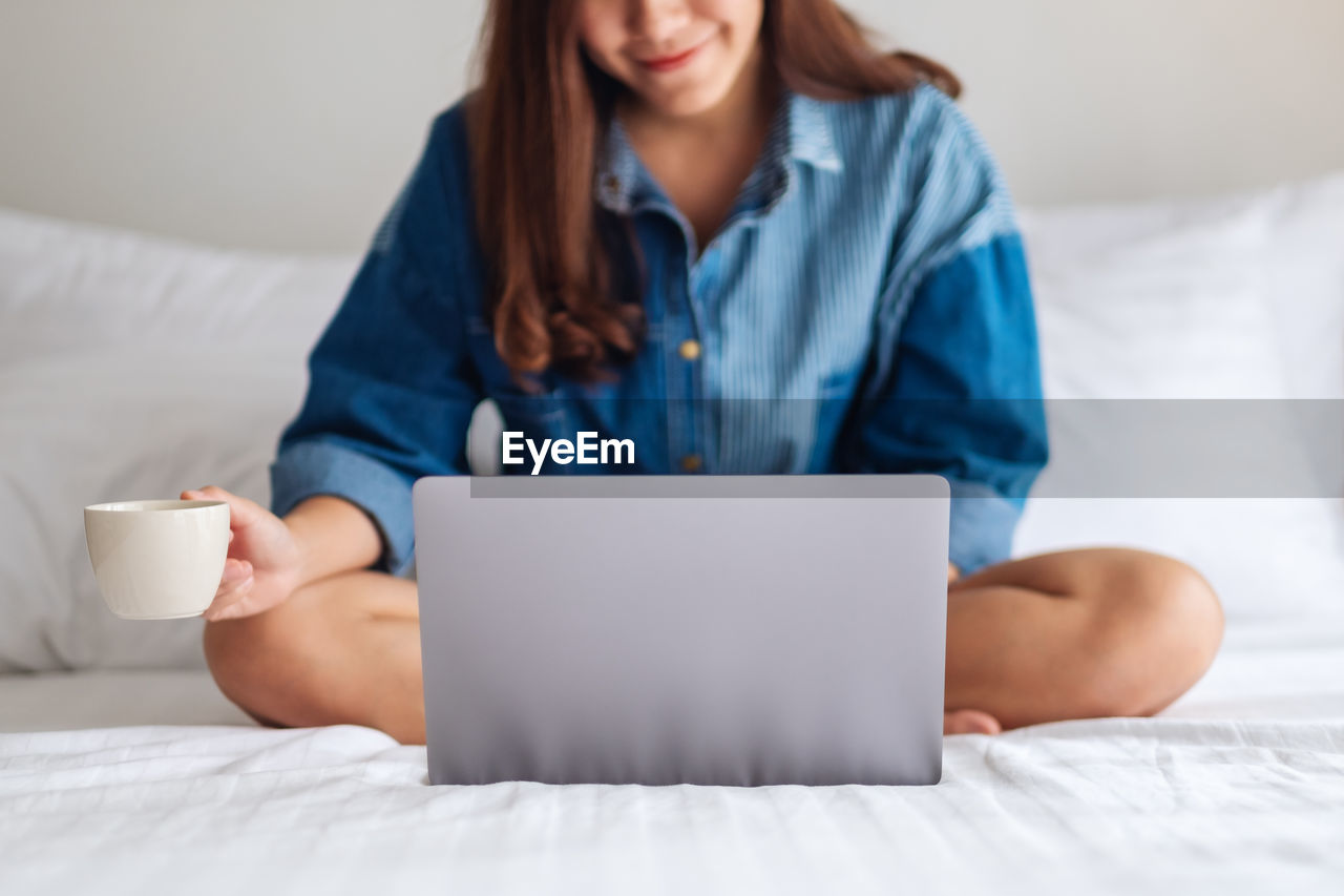 midsection of woman using laptop while sitting on bed at home