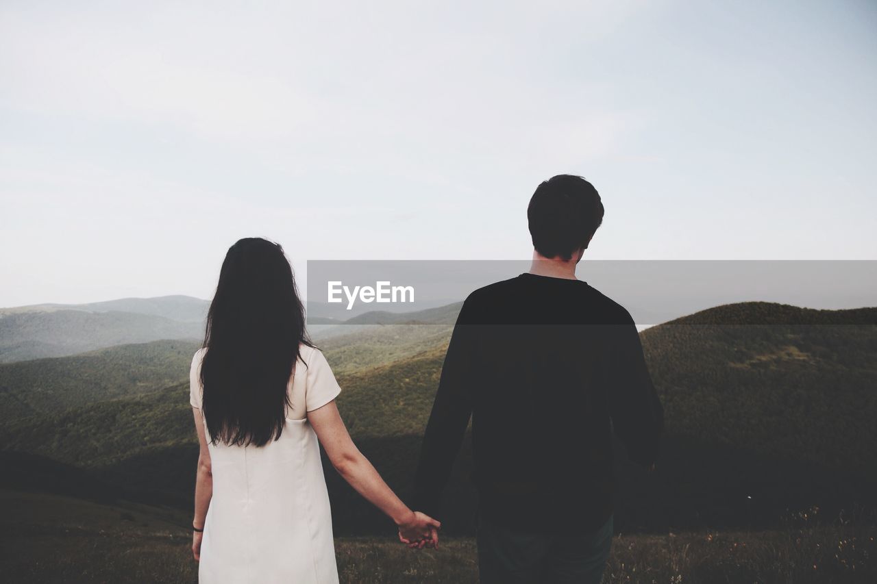 Young couple holding hands and looking at scenic view in mountains