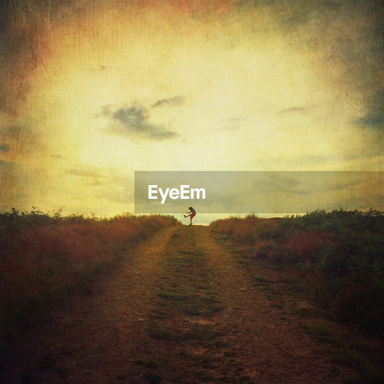 Distant view of person jumping on dirt road against sky