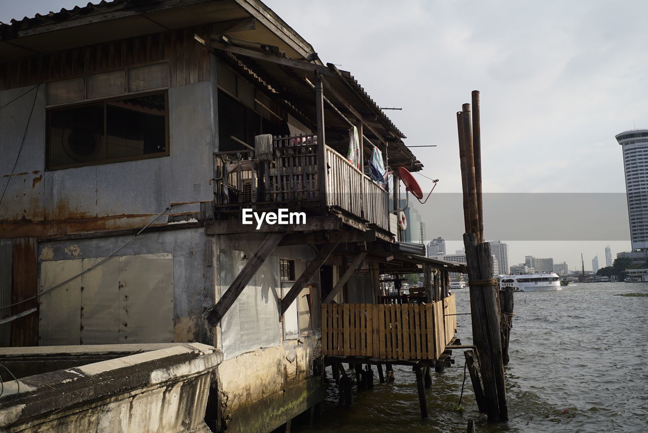 Abandoned building by river in city against sky