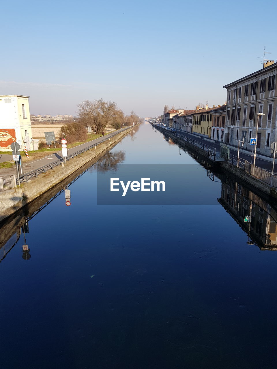 Reflection of buildings in canal against clear blue sky