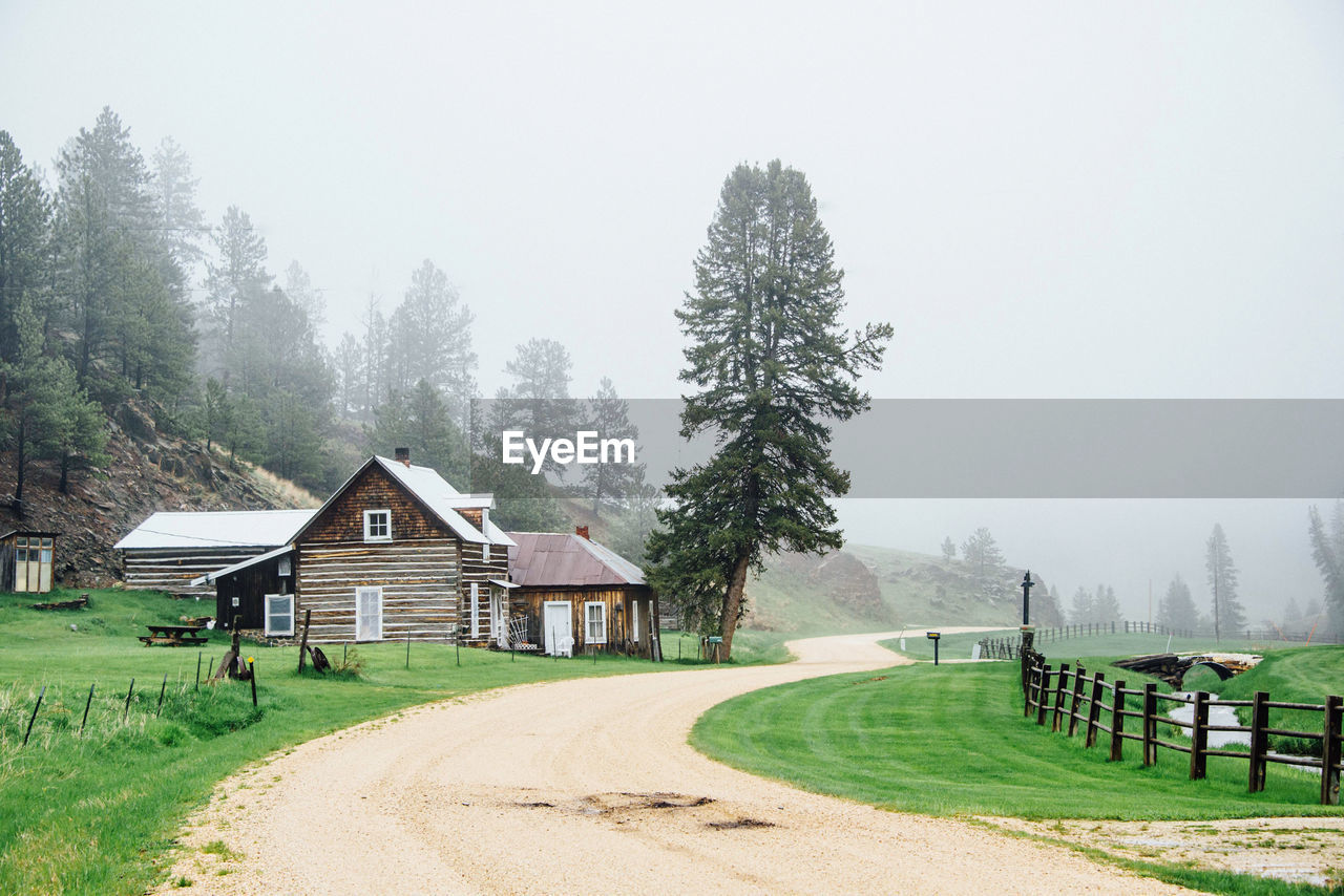 Cabin amidst trees and buildings against foggy sky