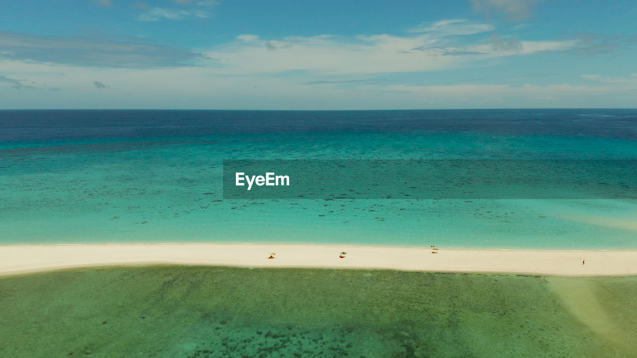 Tropical white island and sandy beach with tourists surrounded by coral reef and blue sea