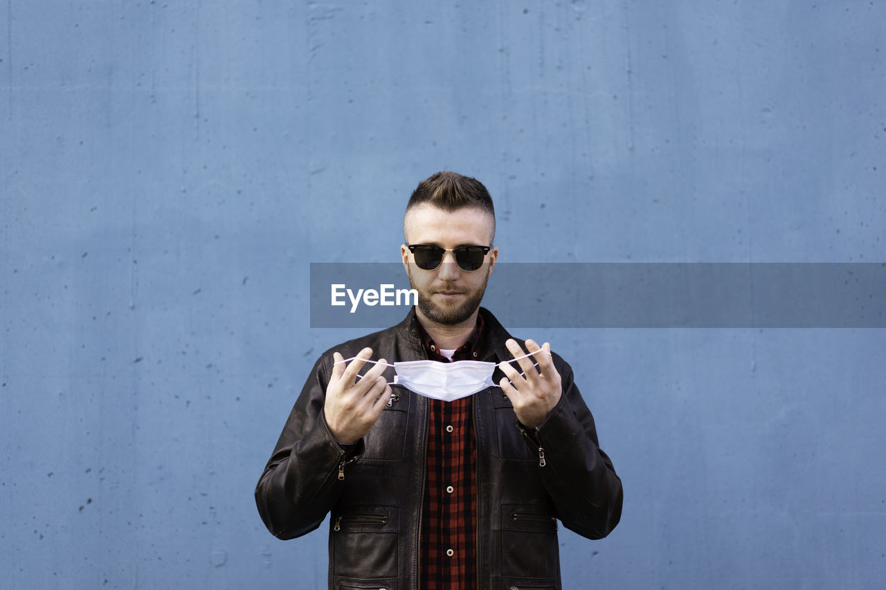 Portrait of young man wearing sunglasses standing against wall