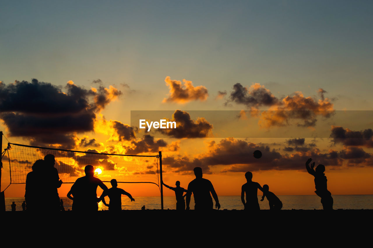 Silhouette people playing volleyball at beach during sunset