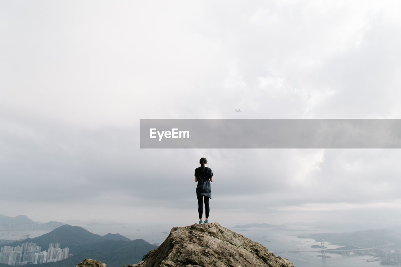 Woman standing on top of mountain against cloudy sky