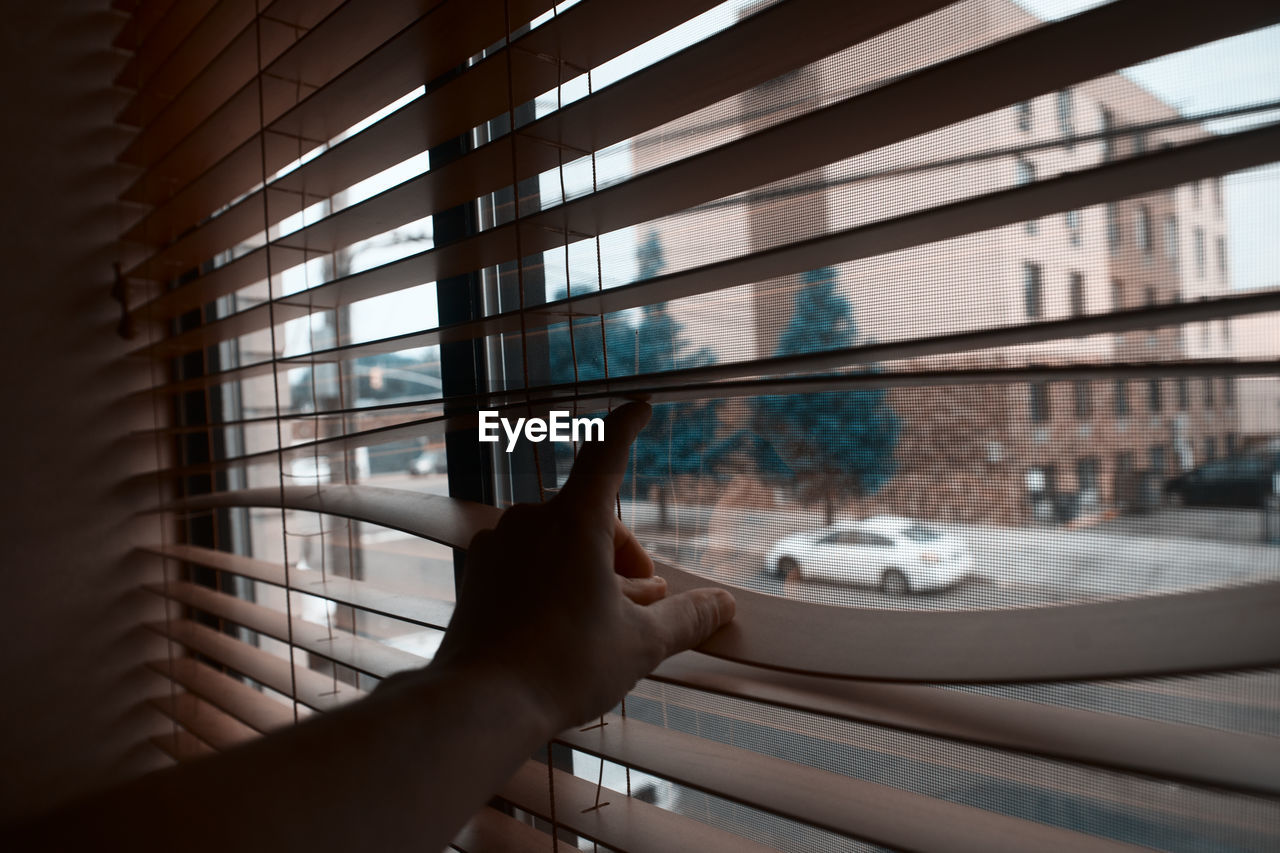 Cropped image of person touching blinds while looking through window