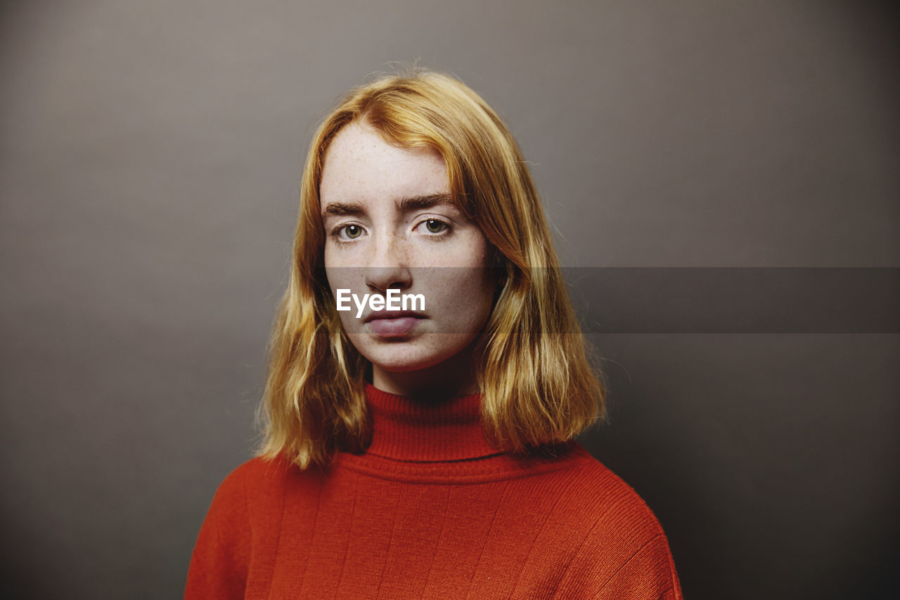 Teenage girl staring while standing against gray background