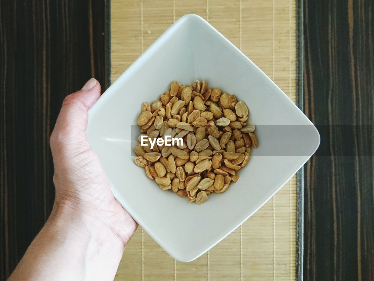 Cropped hand holding peanuts in bowl over table