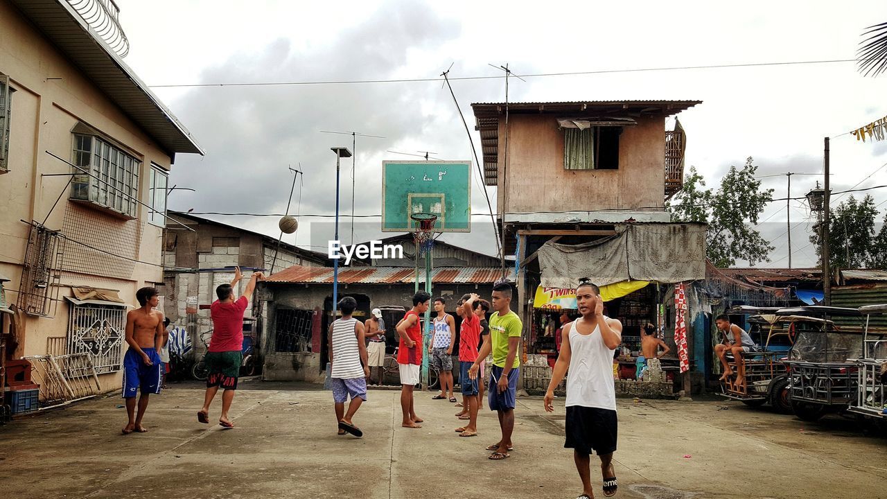 PEOPLE WALKING ON STREET AMIDST BUILDINGS AGAINST SKY