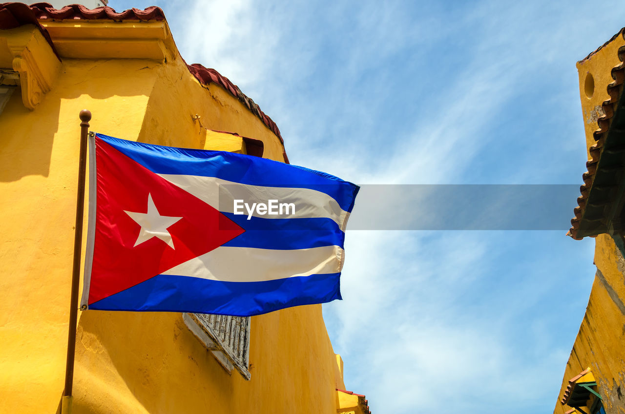 Low angle view of cuban flag and yellow building against sky