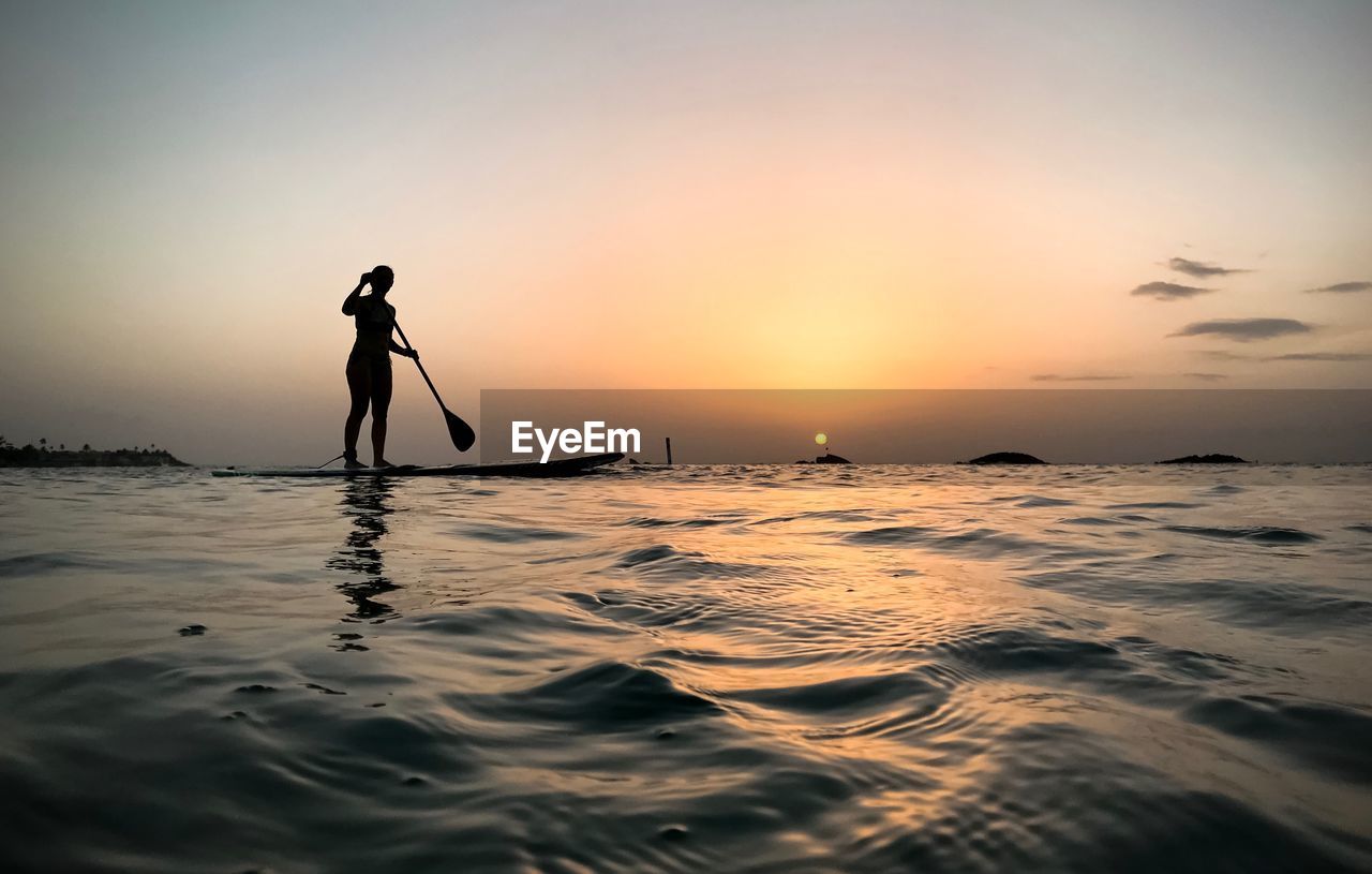 SILHOUETTE MAN STANDING ON SHORE AGAINST SKY DURING SUNSET