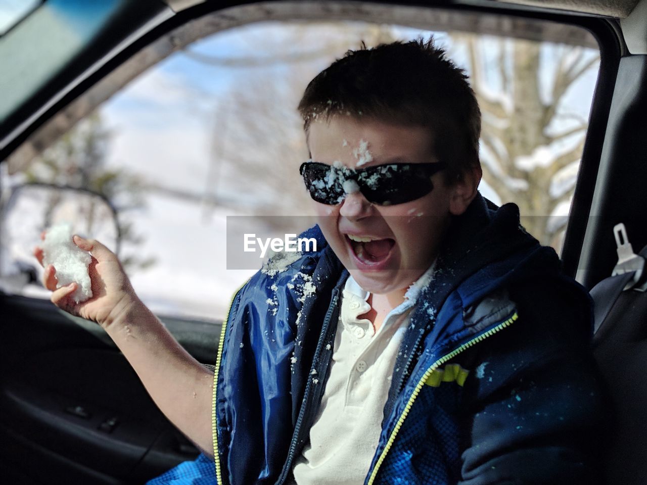 Portrait of boy shouting while sitting with snow in car