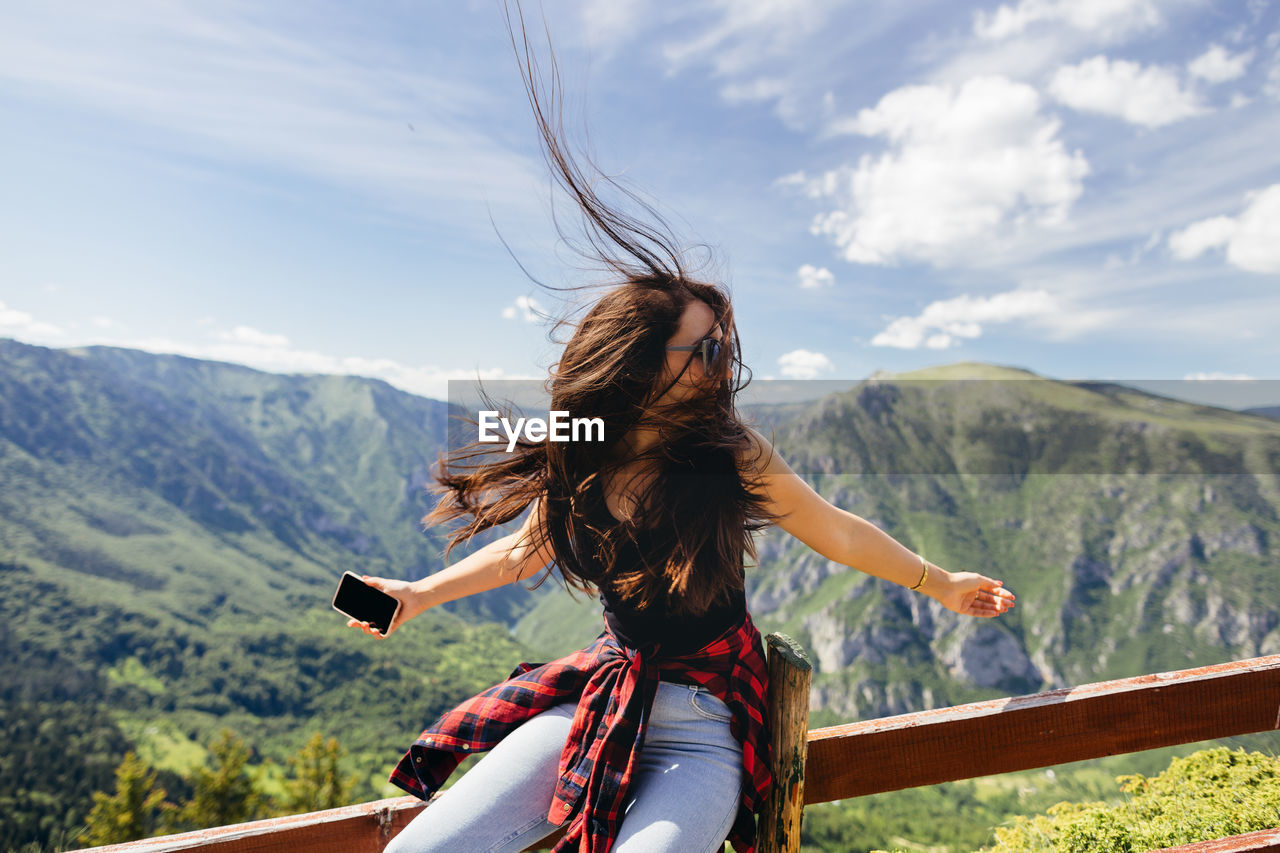 Woman with arms raised on mountain against sky