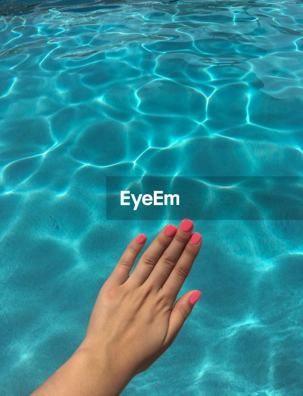 Cropped hand of woman showing nail polish over swimming pool