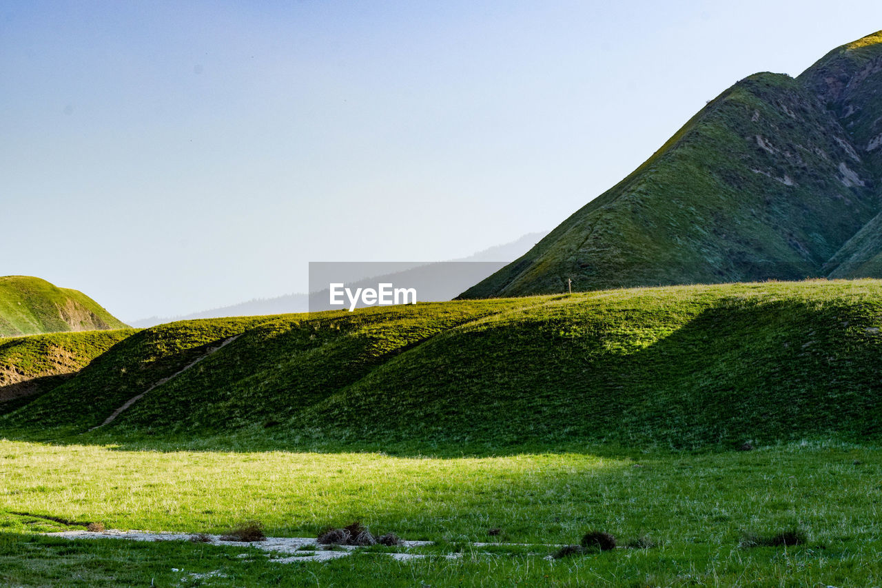 Scenic view of grassy field by mountain against clear sky