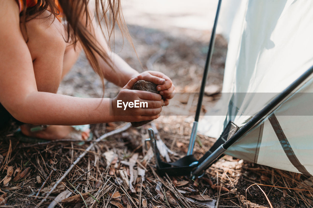 Cropped image of girl hitting stone on tent peg at campsite