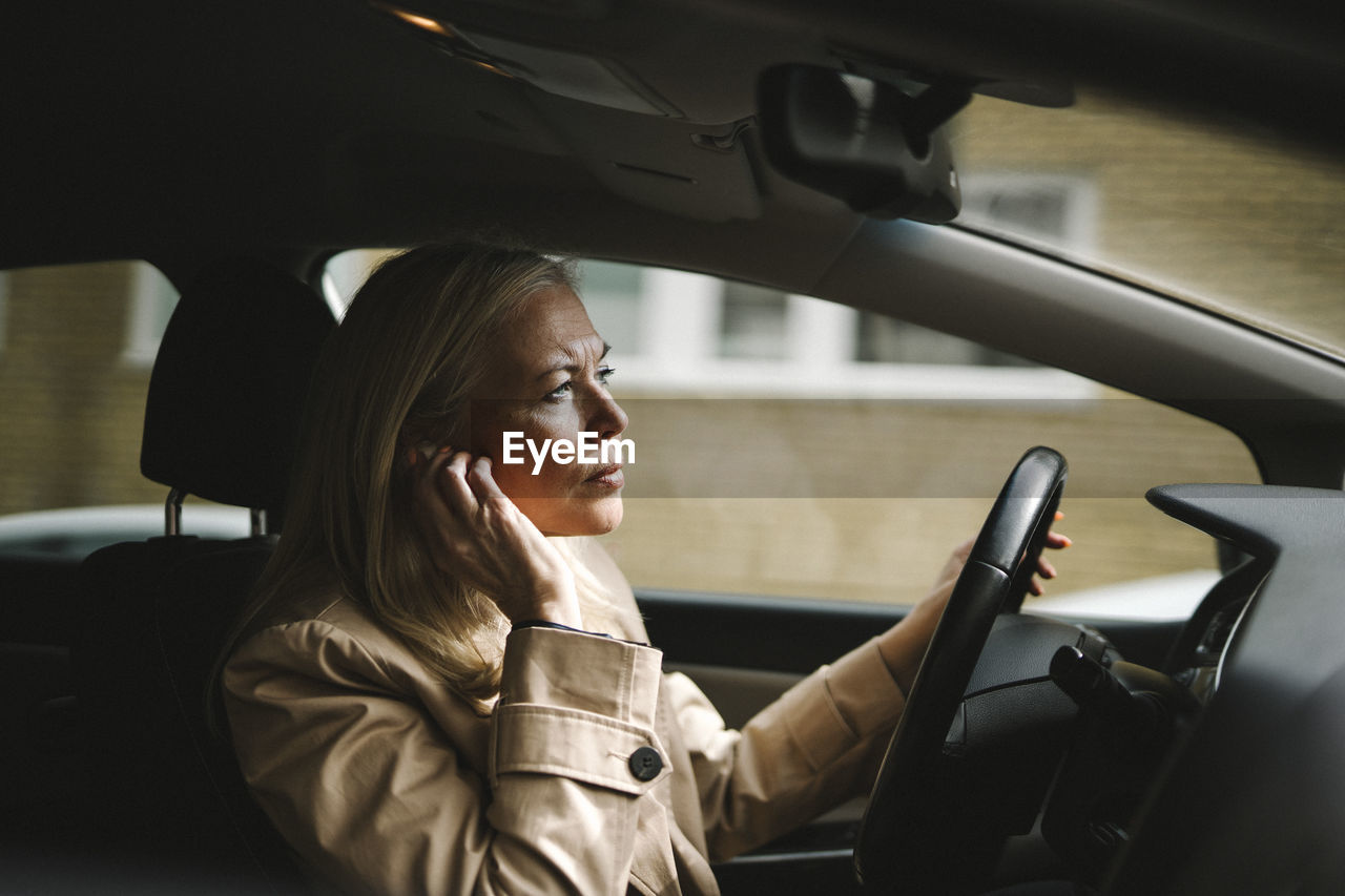 Businesswoman adjusting in-ear headphones while driving car