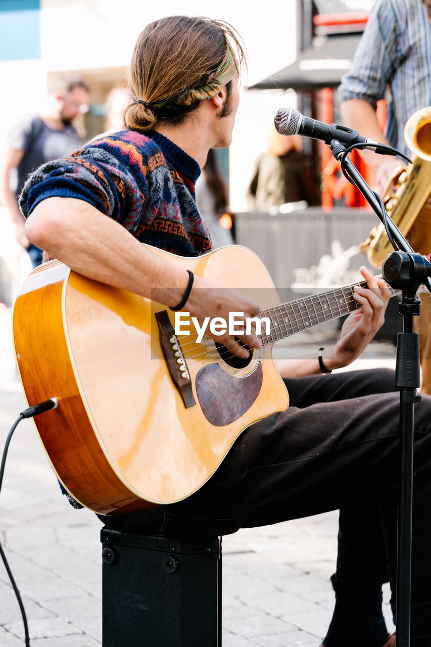 Man with tied long hair singing and playing a guitar in the street