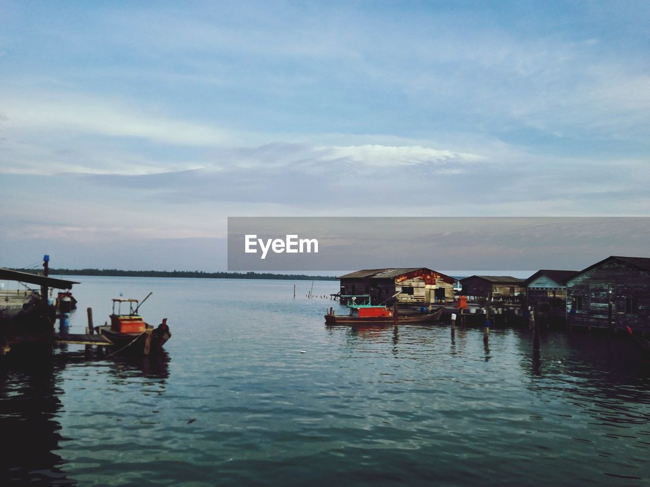 Boats and houses on sea against cloudy sky