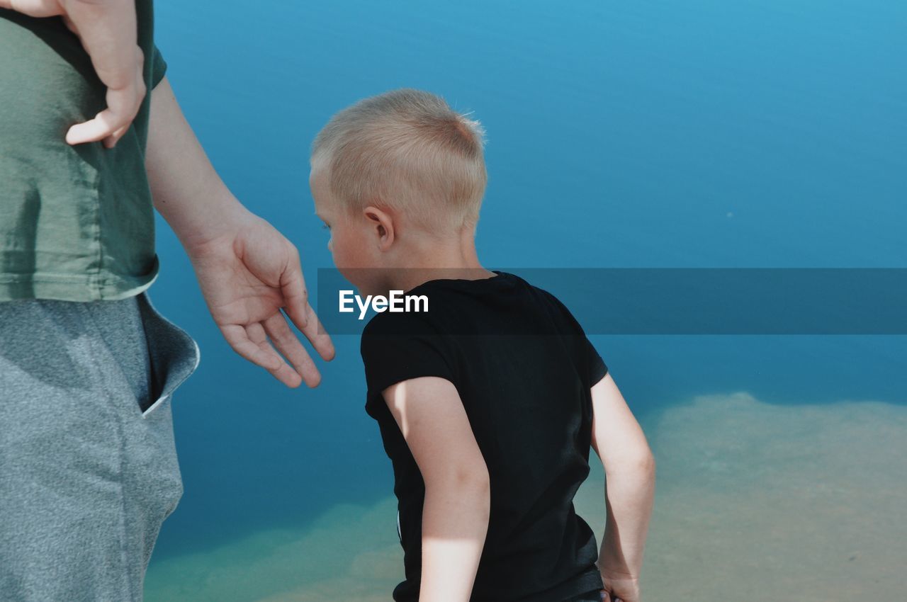 REAR VIEW OF FATHER AND SON STANDING AT SHORE