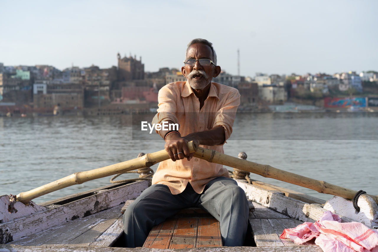 YOUNG MAN SITTING ON BOAT AT RIVER