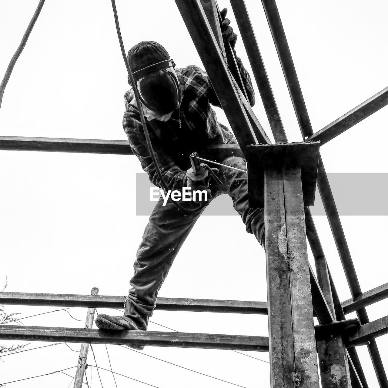 Low angle view of worker working on built structure against clear sky