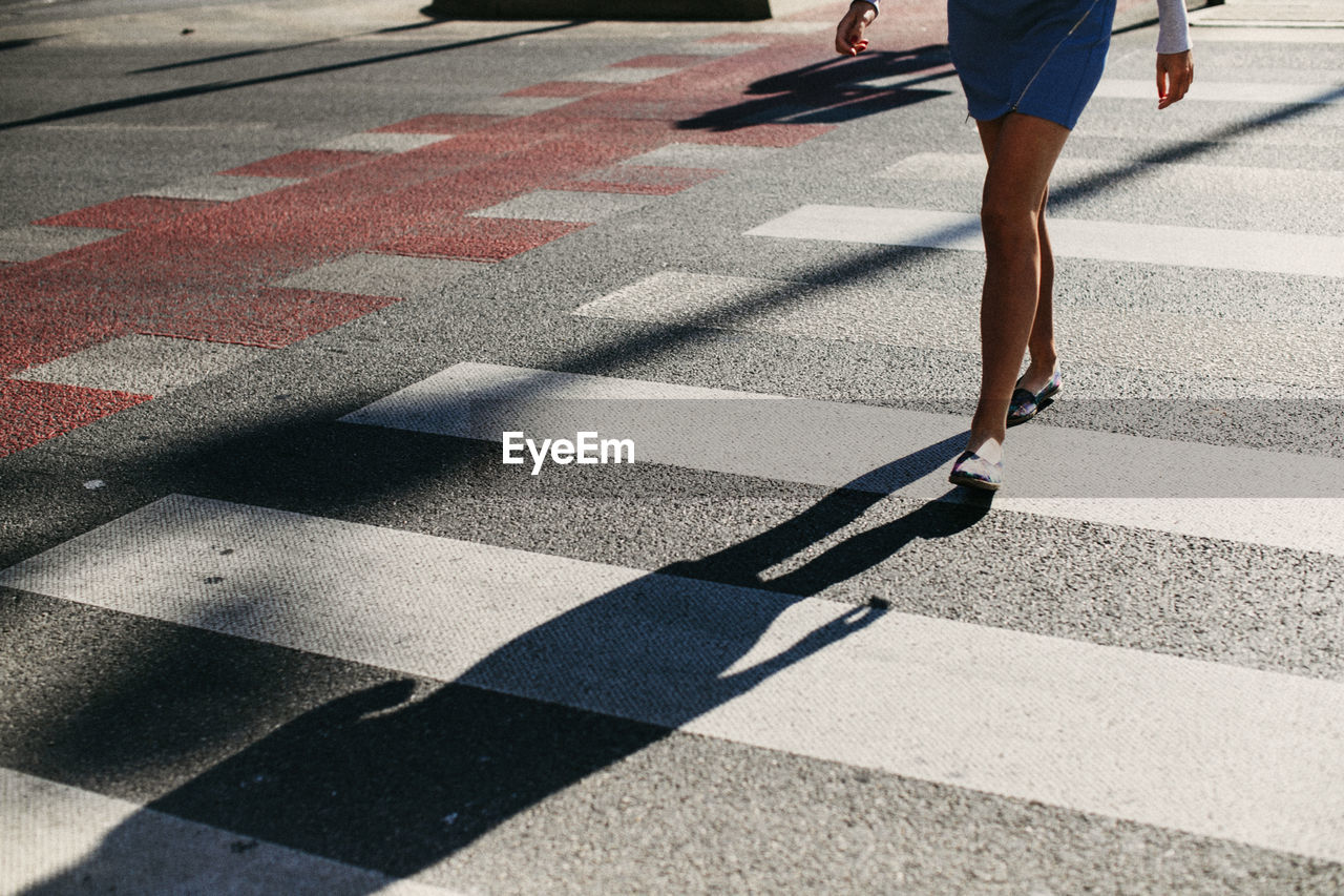 Low section of woman crossing road in city