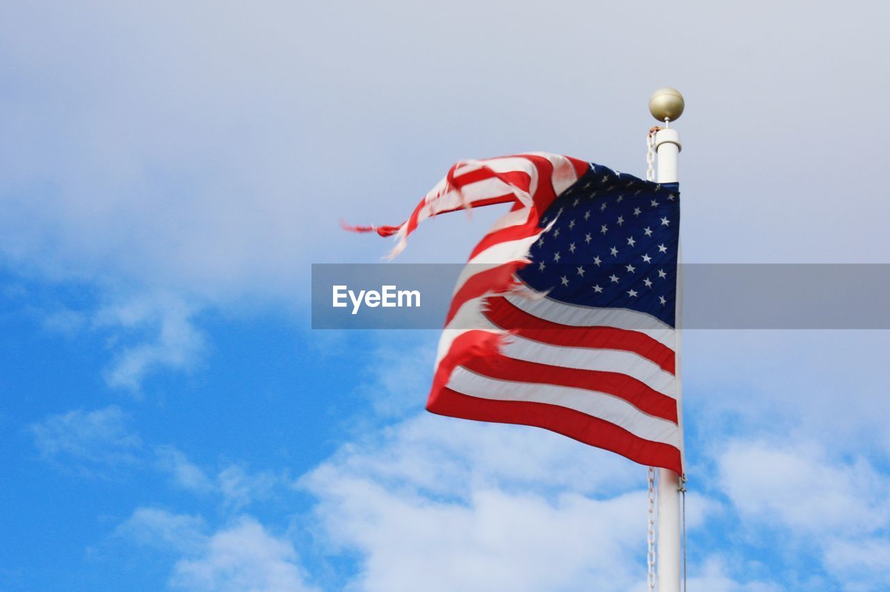 Low angle view of torn american flag fluttering against cloudy sky
