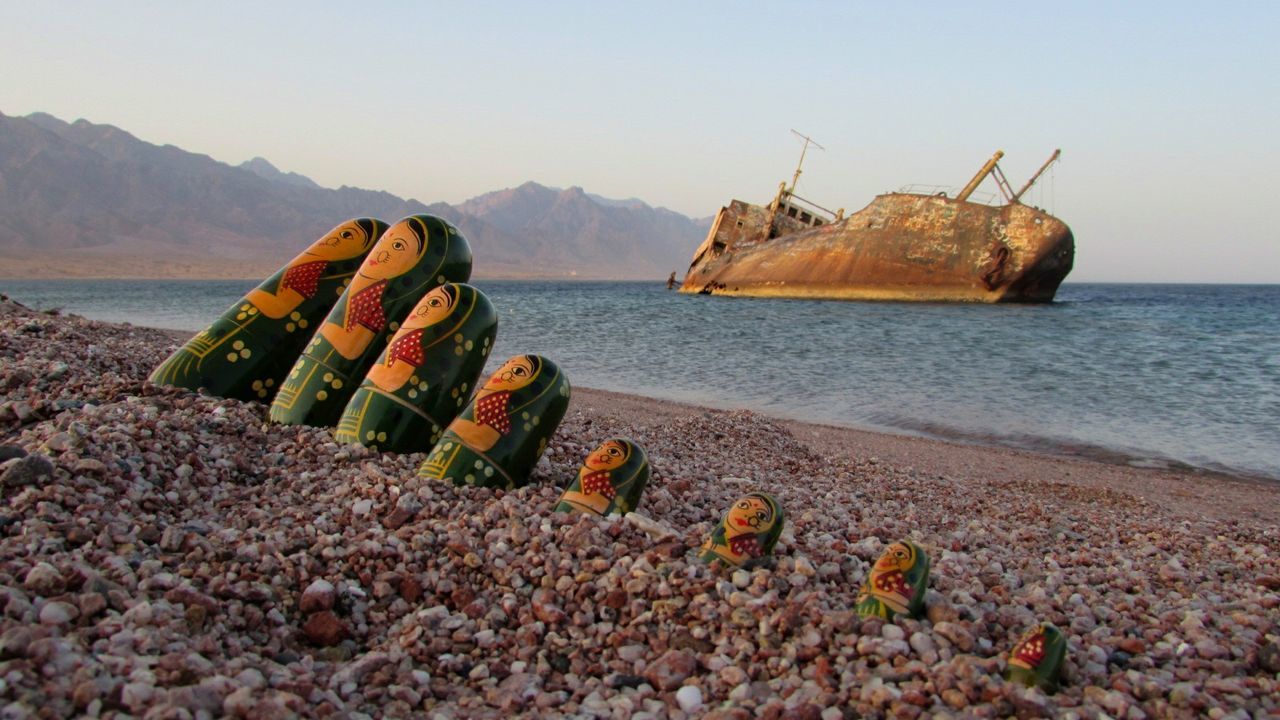 Dolls on sea shore with shipwreck in background