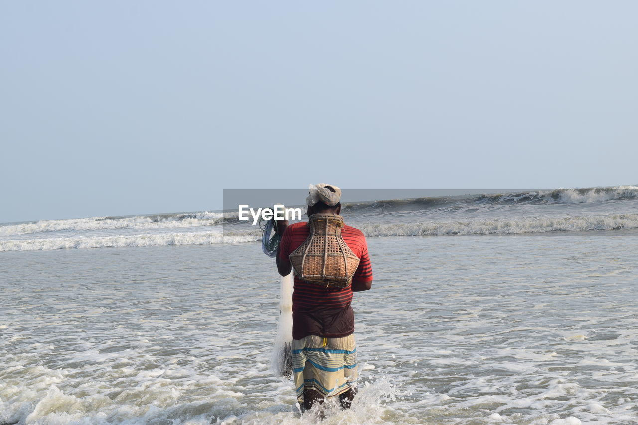 REAR VIEW OF MAN STANDING ON BEACH