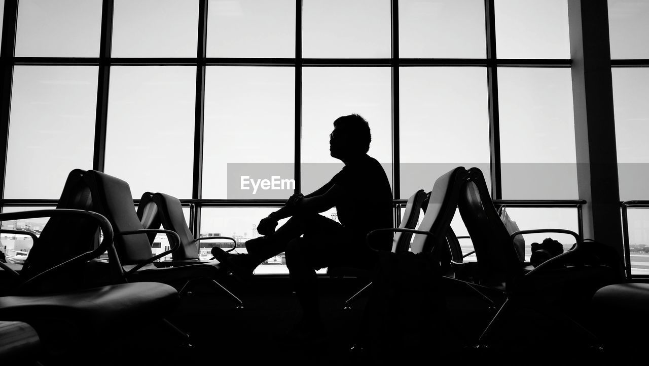 Silhouette man sitting against window at airport