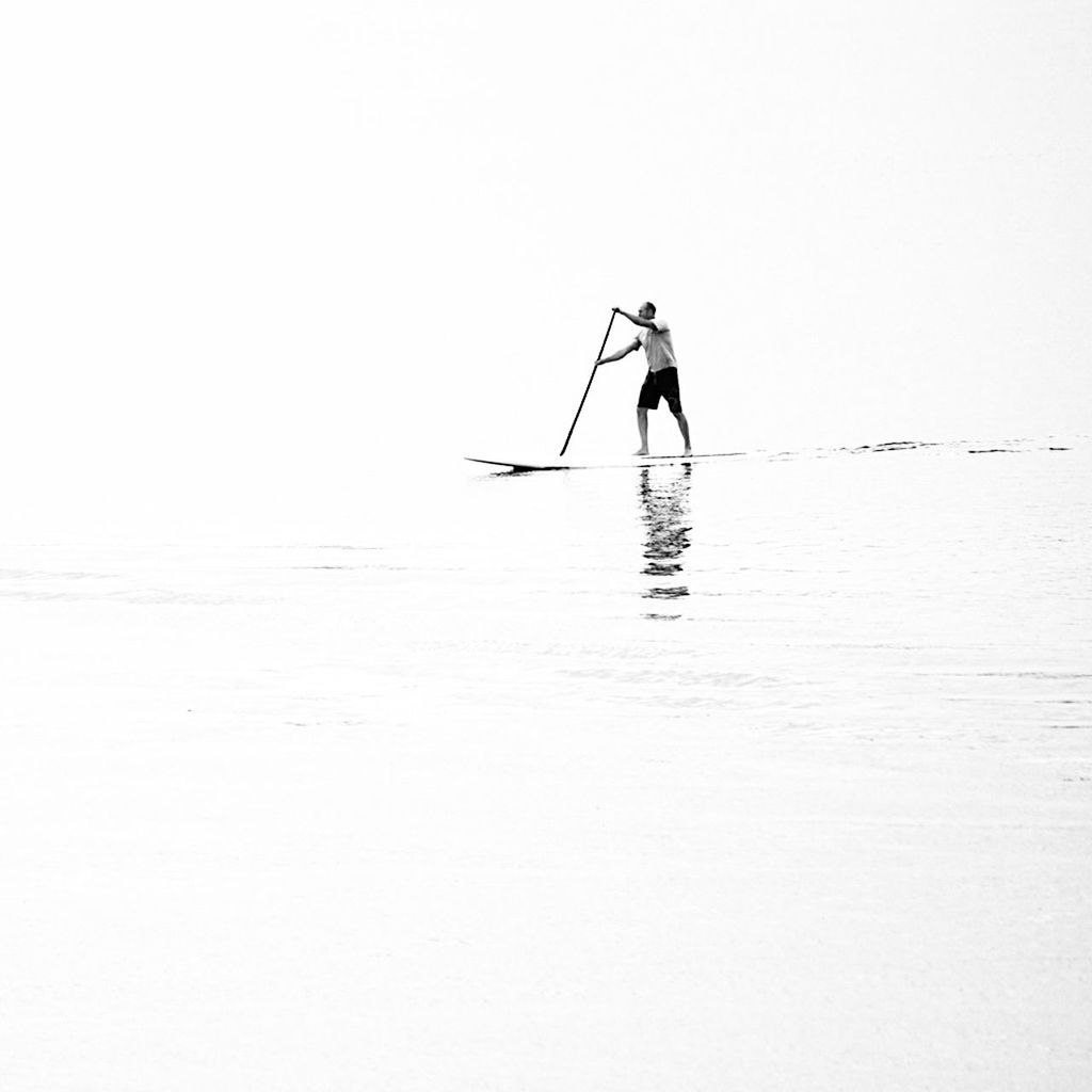 Man paddleboarding on sea against clear sky