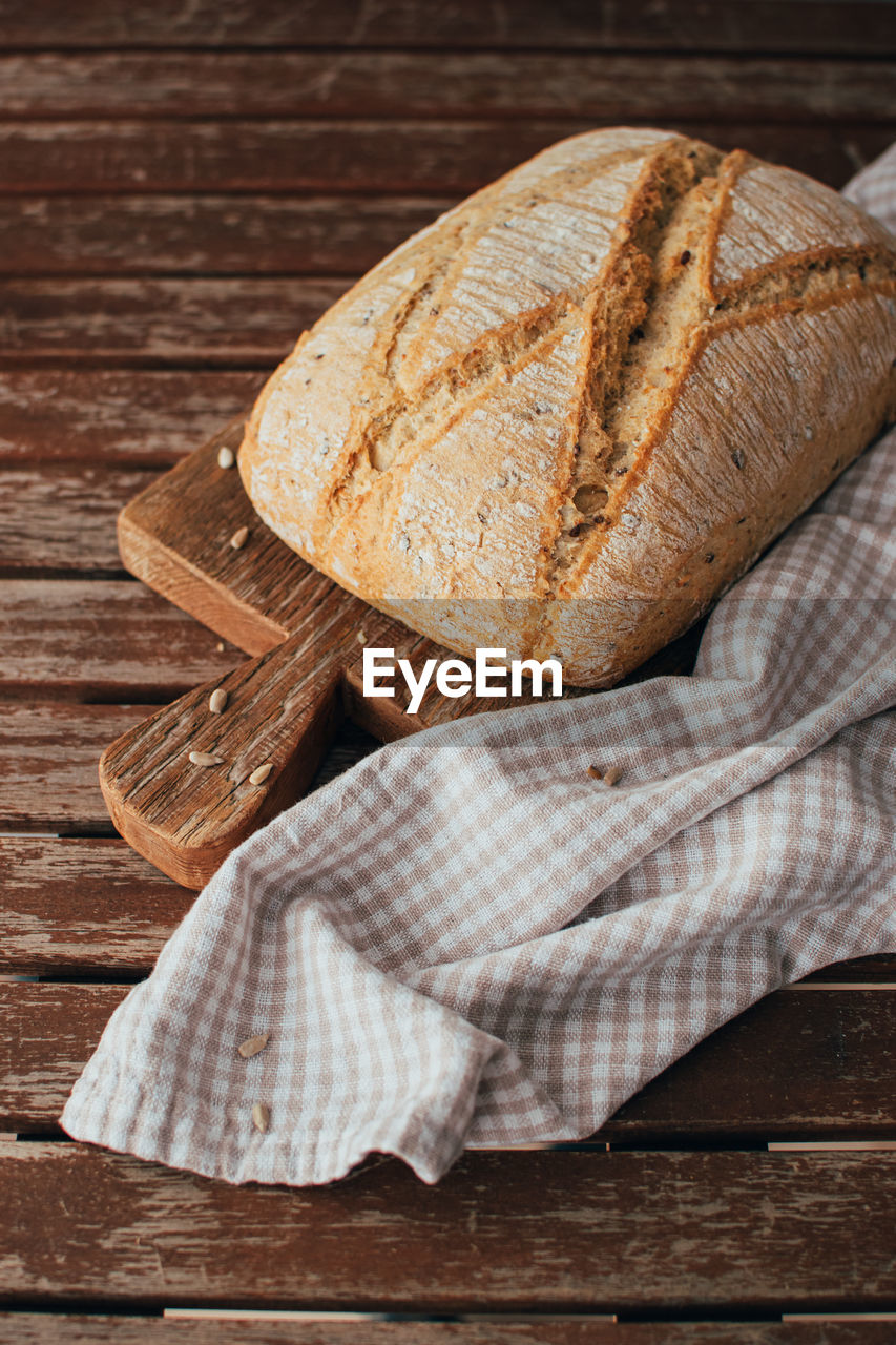 Freshly baked bread loaf on rustic wooden cutting board and napkin