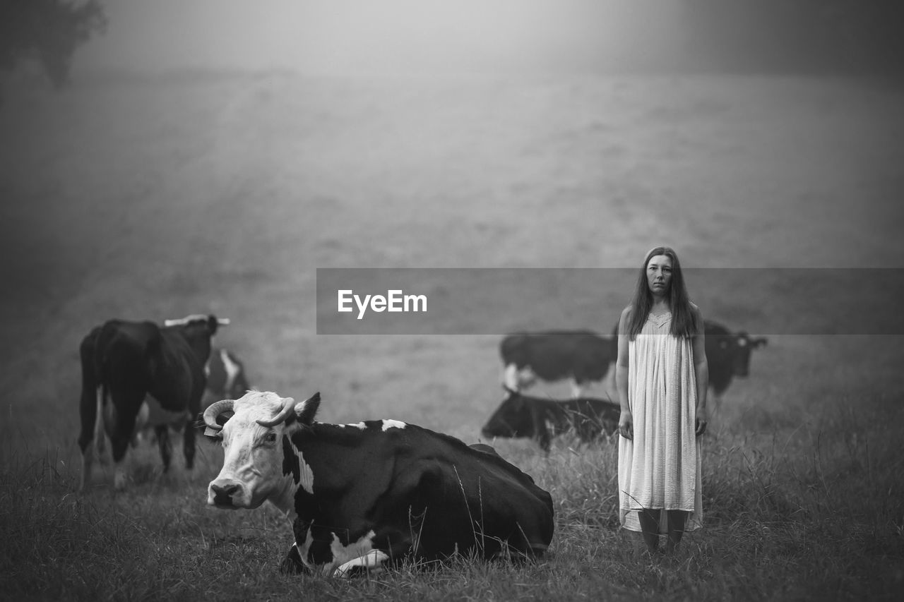 Portrait of woman standing with cows on field during foggy weather