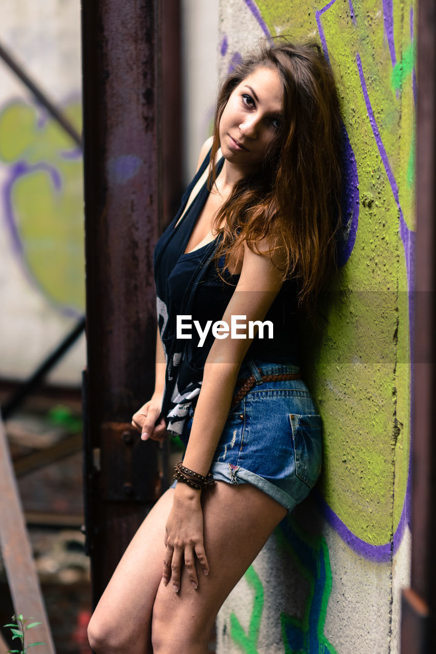 SIDE VIEW OF WOMAN STANDING AGAINST GRAFFITI WALL