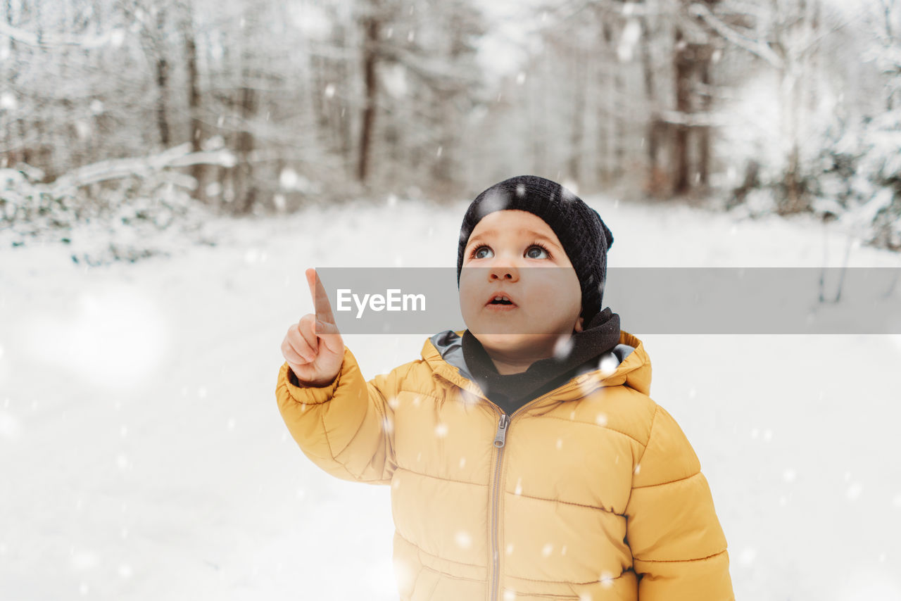 Cute boy pointing while standing on snow during winter