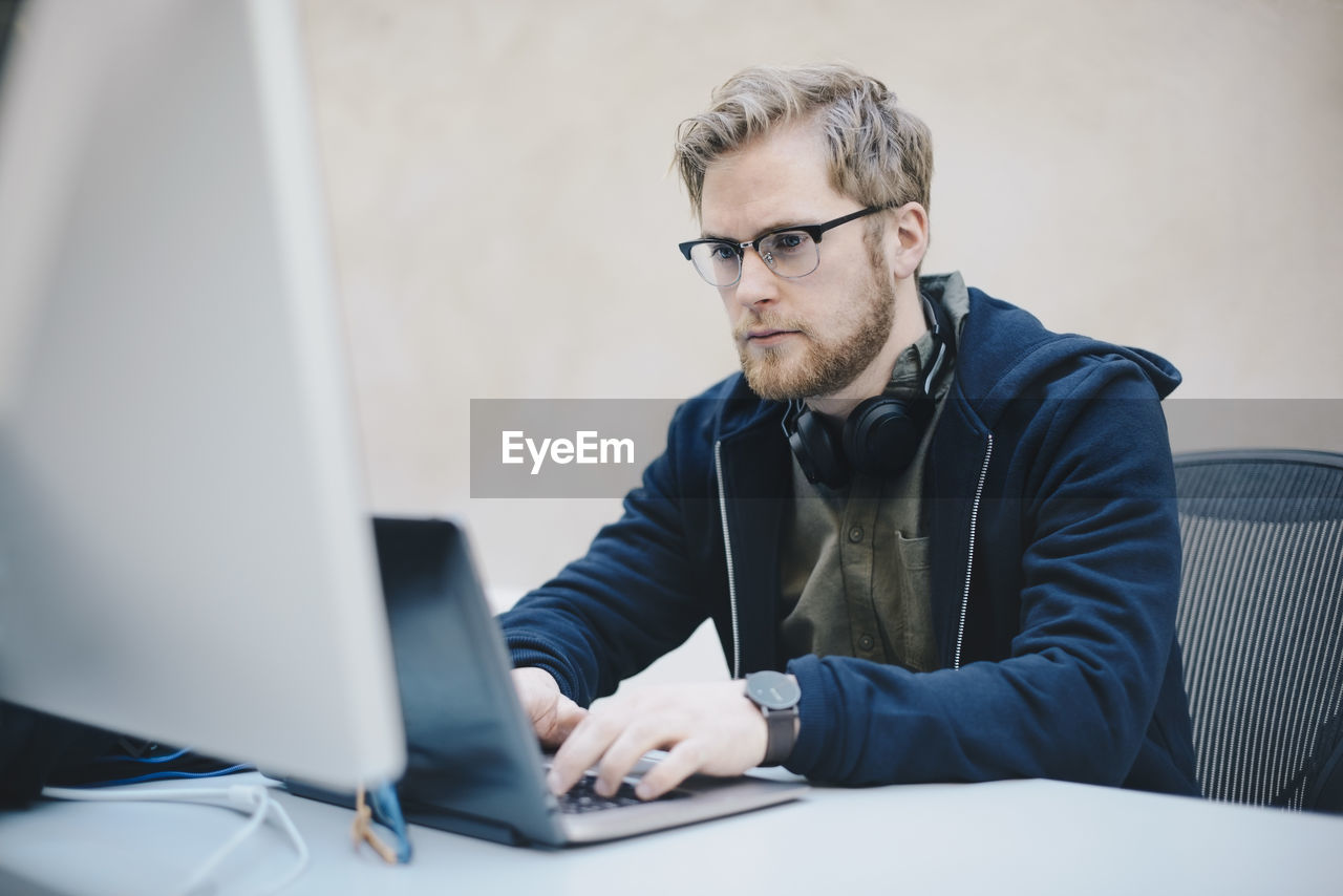 Male computer programmer using laptop at desk in office