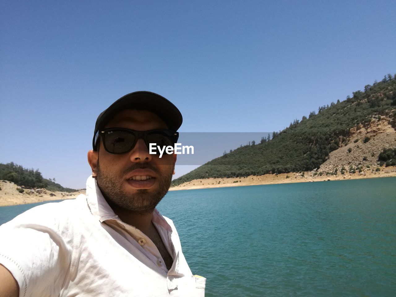 PORTRAIT OF YOUNG MAN WEARING SUNGLASSES STANDING AGAINST SKY