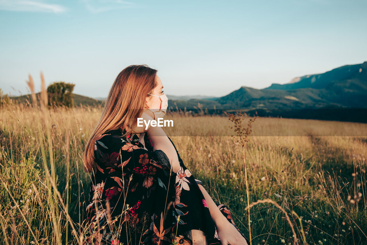 Young woman standing on field against sky