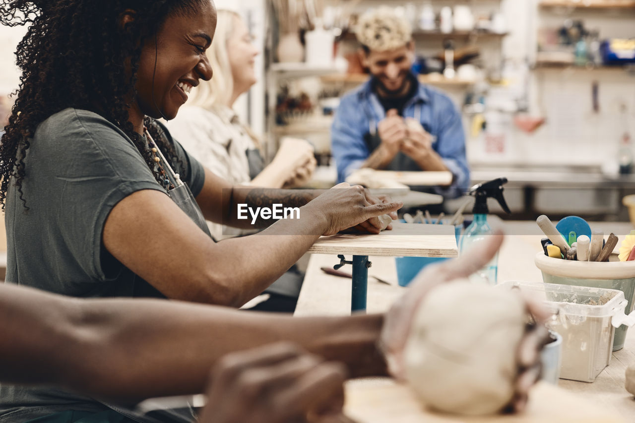 Cheerful mature woman molding clay while practicing in art class